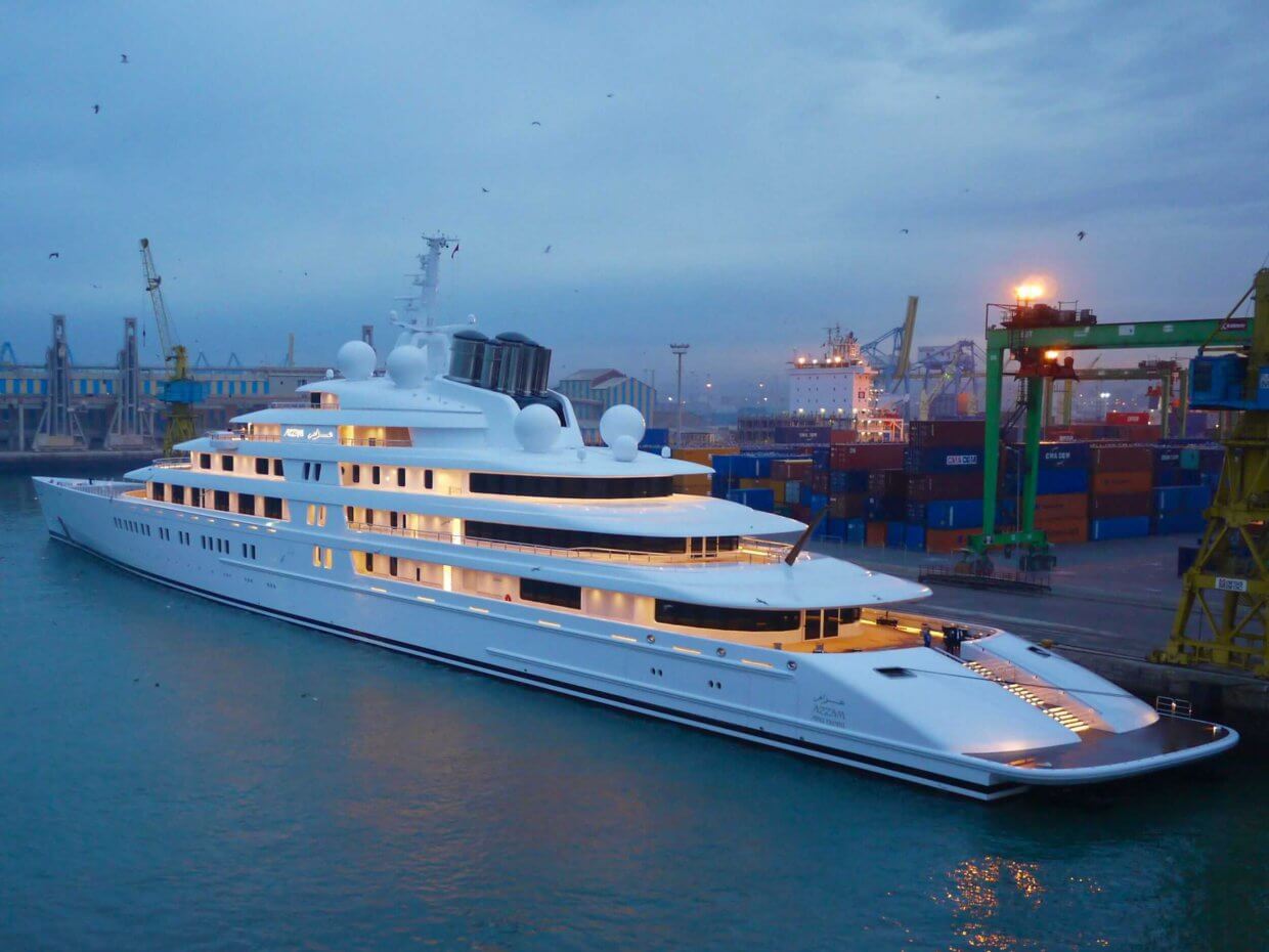 Luxury yacht docked in a port with illuminated decks, surrounded by shipping containers and cranes, showcasing advanced marine automation and power management systems relevant to Tess Electrical LLC's services.