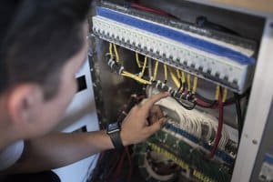 Person inspecting marine electrical wiring and connections inside a control panel, emphasizing yacht electrical systems and maintenance.
