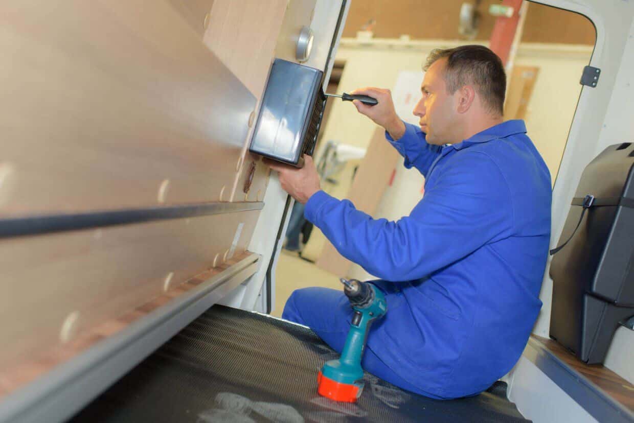 Technician in blue uniform installing marine electrical equipment in yacht interior, showcasing expertise in electrical services for yachts and megayachts.