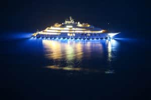 Luxury yacht illuminated at night, showcasing marine electrical systems and lighting effects on water, relevant to marine electrical supplies and yacht ownership.