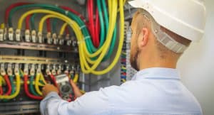 Electrician in hard hat using a multimeter on marine electrical panel with colorful wiring, representing marine electrical services and expertise at Tess Electrical LLC.