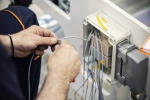 Person working on marine electrical systems, connecting wires to a control panel, emphasizing yacht electrical maintenance and safety.