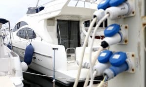 Marina power pedestal with blue electrical outlets connected to a luxury yacht, illustrating marina electrical systems and maintenance.