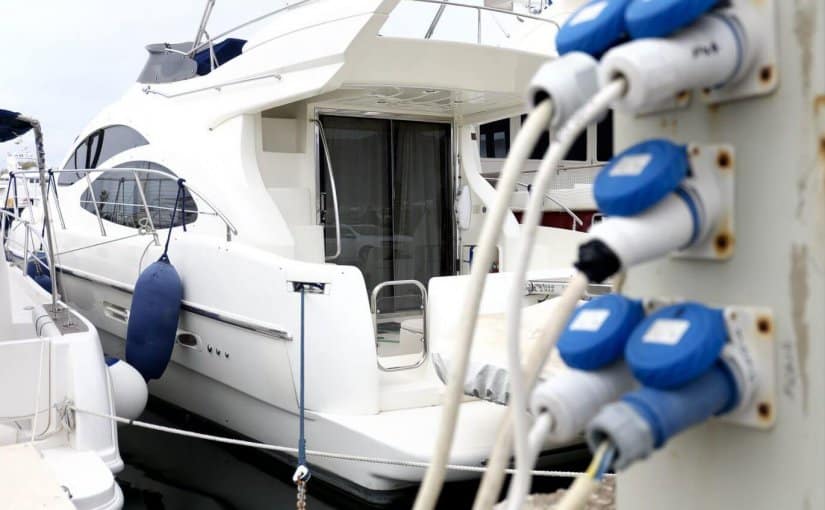 Yacht docked at marina with blue electrical power pedestals and cables, showcasing marina electrical equipment for upgrading facilities.