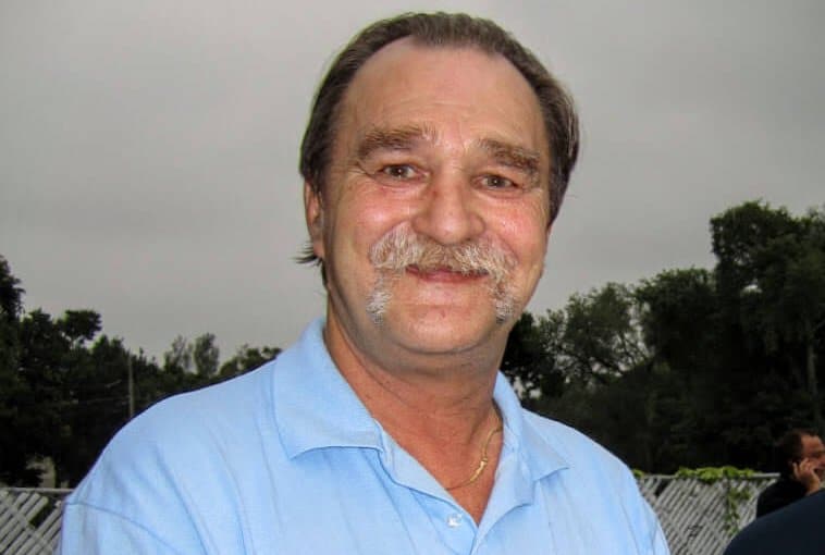 Smiling man with a mustache wearing a light blue shirt, commemorating Frank Salenieks, a cherished friend known for his unique personality and love for animals.