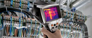Hand holding an infrared camera aimed at electrical panels, showcasing thermographic analysis for marine electrical systems and safety.