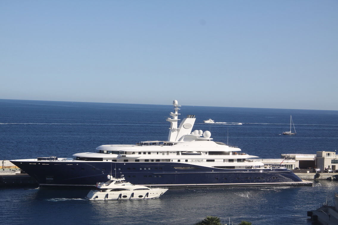 Luxury yacht Al Miqrab, owned by Qatar's former Prime Minister, featuring a sleek design, moored in a harbor with surrounding water and smaller boats.