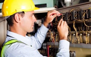 Electrician performing maintenance on yacht electrical systems, wearing safety helmet and reflective gear, focused on wiring and circuit connections.