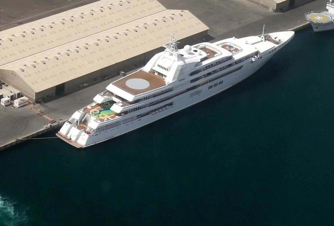 Luxury yacht Dubai docked at a harbor, showcasing its sleek design and spacious deck with a swimming pool, helicopter pad, and lavish amenities.