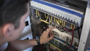 Person inspecting marine electrical panel with wires and connections, highlighting maintenance for marina electrical systems.