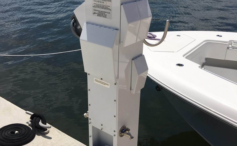 Dock power pedestal with integrated features for marina electrical services, showcasing safety enhancements and modern design, adjacent to a boat and water.