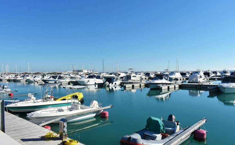 Marina filled with various boats and yachts reflecting in calm water, highlighting the importance of electrical safety and maintenance in marine environments.