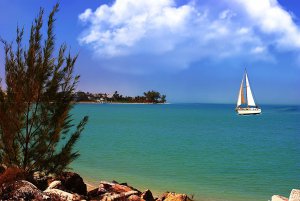 Sailboat navigating calm turquoise waters with a scenic shoreline and blue sky, representing ideal boating experiences and destinations for yacht owners.