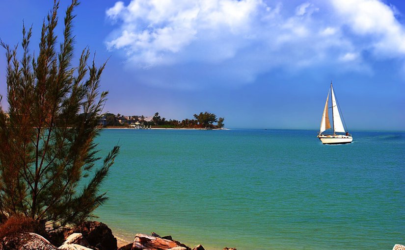Sailboat cruising on turquoise waters near a coastal landscape, highlighting Florida's Gulf Coast boating destinations.