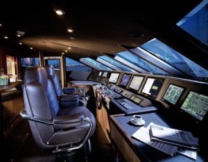 Interior view of a luxury yacht's control room featuring modern navigation equipment, two ergonomic captain's chairs, and large windows providing natural light, emphasizing advanced marine technology and power management systems like GENSYS 2.0 MARINE.