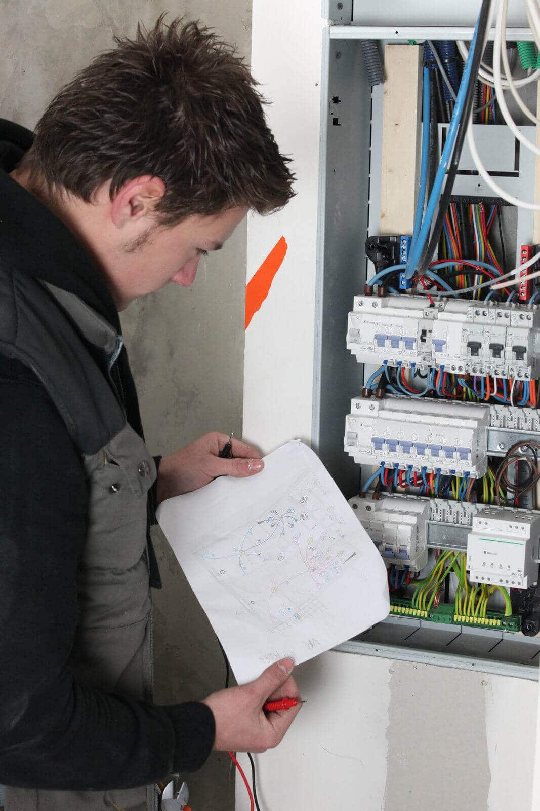 Electrician examining electrical panel with schematic diagram, highlighting marine electrical refit services relevant to yacht maintenance and renovation.