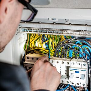 Marine electrician working on yacht electrical panel with colorful wiring and circuit breakers.