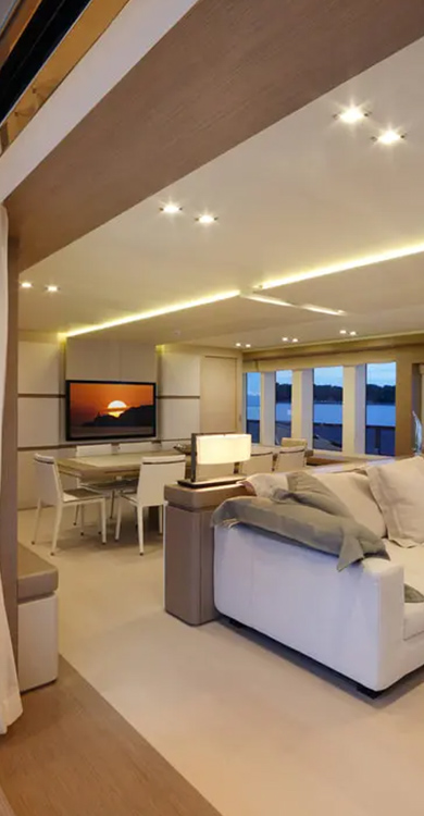 Luxurious yacht interior featuring modern Cantalupi lighting, elegant dining area, plush seating, and panoramic windows showcasing a sunset view.