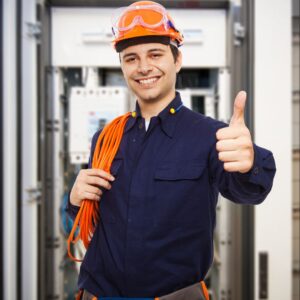 Smiling marine electrician giving a thumbs up, wearing safety gear and holding electrical cables, in front of yacht electrical systems, representing Tess LLC's on-demand marine electrical services.