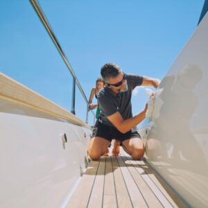 Man cleaning the exterior of a yacht, emphasizing regular maintenance for optimal vessel condition and safety.