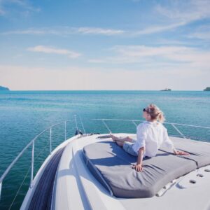 Person relaxing on yacht deck overlooking calm blue waters, emphasizing luxury and leisure in marine settings.