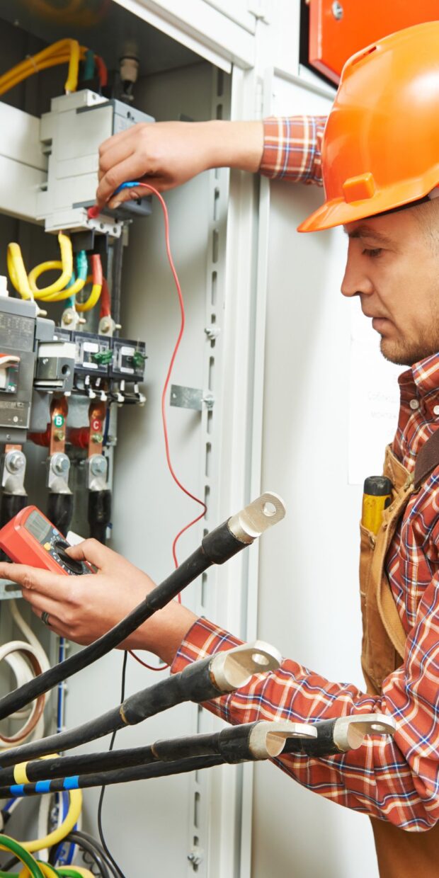 Electrician in safety gear using a multimeter to test electrical connections in a yacht's electrical panel, showcasing expertise in marine electrical services for Broward County.