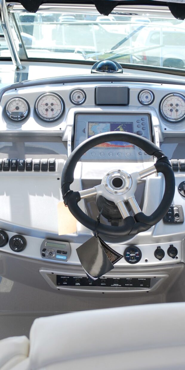 Yacht cockpit dashboard featuring steering wheel, navigation display, and control panels for marine electrical systems.