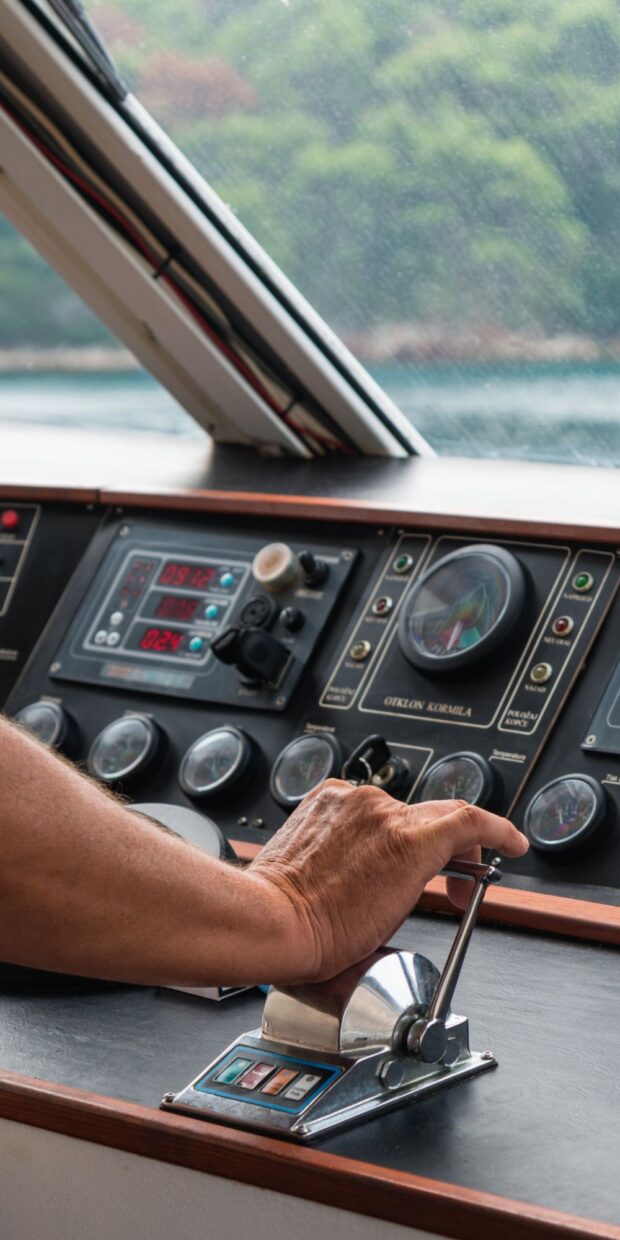Hand operating yacht control lever at the helm, with gauges and electronic displays in the background, emphasizing marine electrical systems and navigation.