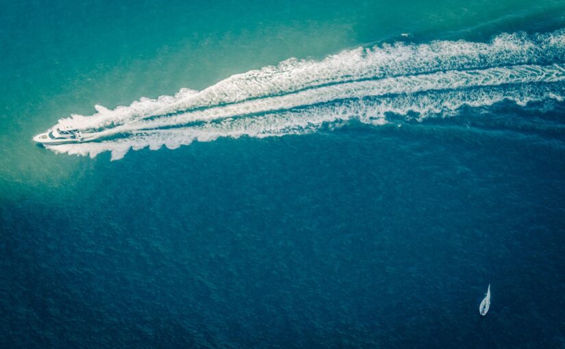 Aerial view of a yacht speeding through turquoise waters, leaving a white wake, emphasizing the importance of yacht safety and security.