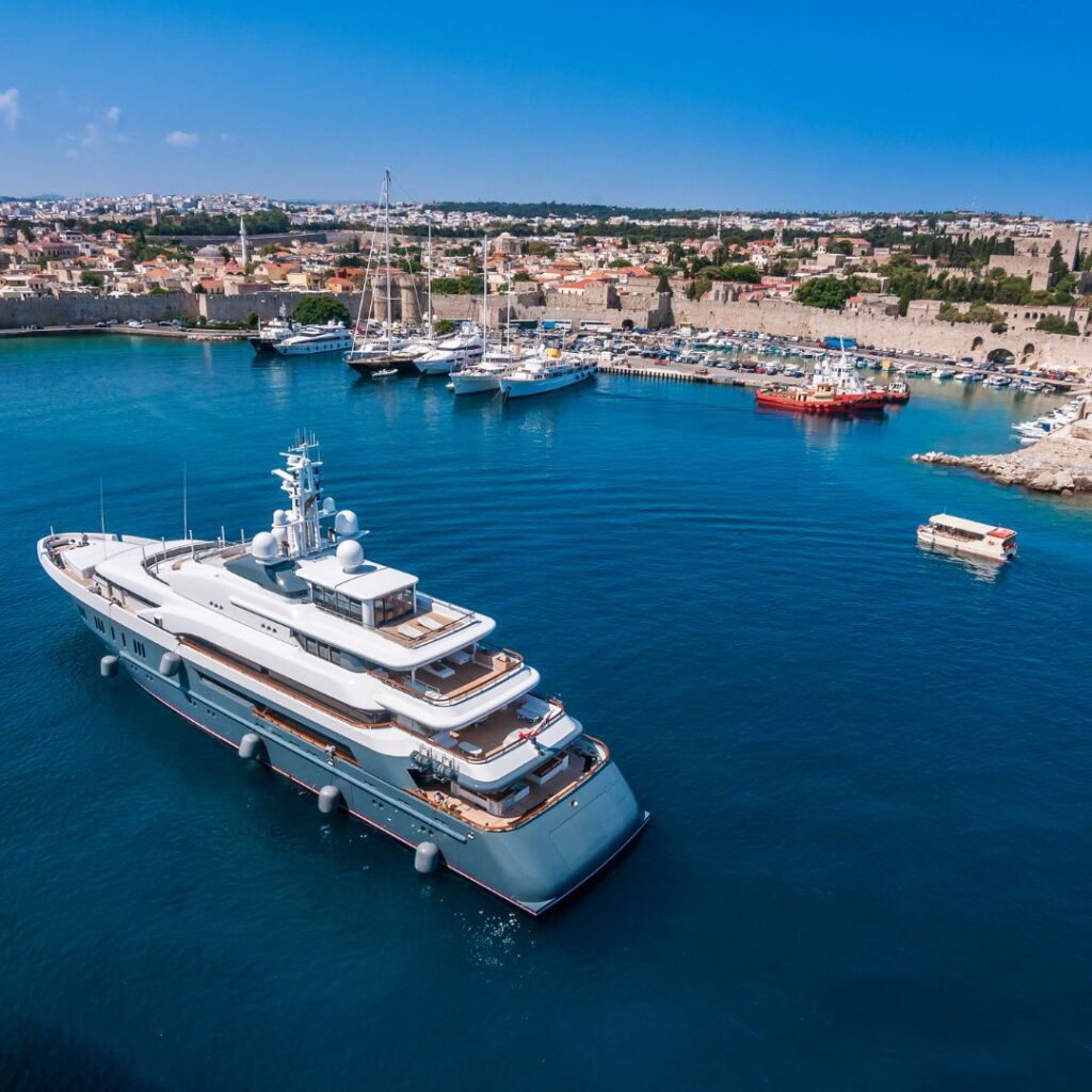 Luxury yacht anchored in a marina with a coastal city backdrop, showcasing advanced marine power management solutions for optimal vessel performance and safety.