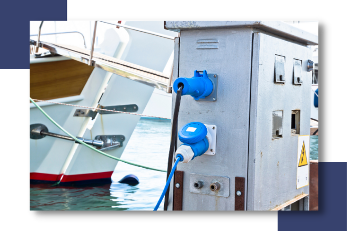 Electrical power connections at a marina with blue plugs and a yacht in the background, highlighting marine electrical systems and reliability for yacht safety.