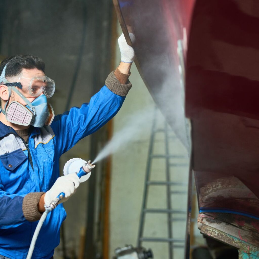 Man in protective gear spraying paint on a yacht during a marine electric refit process, showcasing yacht maintenance and repair expertise.