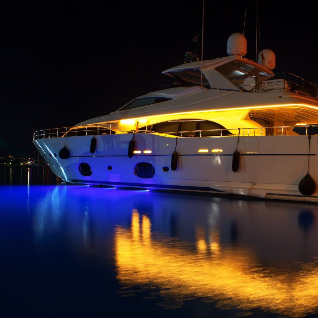 Luxury yacht illuminated at night with vibrant blue and orange lights reflecting on calm water, showcasing advanced marine design and aesthetic appeal, relevant to yacht power system upgrades and energy efficiency.