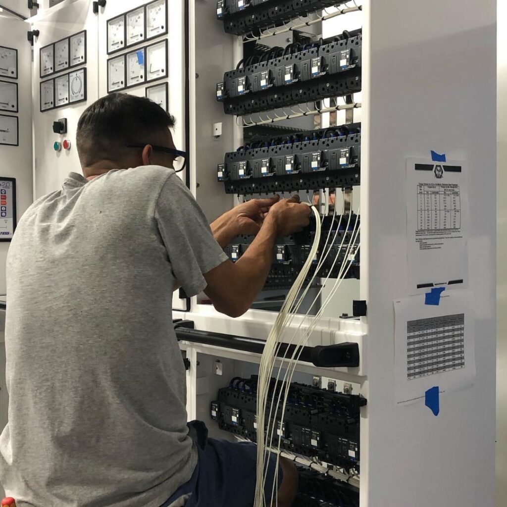 Technician performing maintenance on yacht power system control panel, adjusting wiring and circuit breakers, emphasizing marine electrical service expertise by TESS LLC.