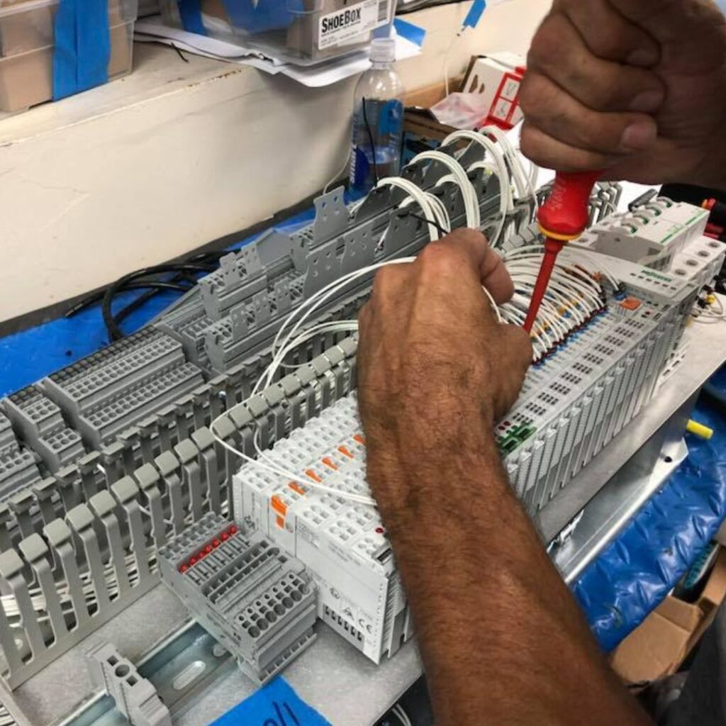 Person using a screwdriver to install electrical components on a marine control panel, emphasizing yacht power system upgrades and maintenance.