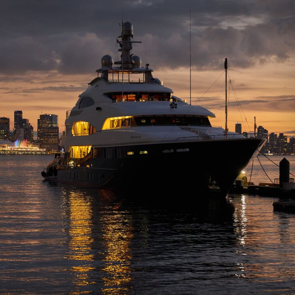 Luxury yacht docked at sunset, showcasing illuminated features and city skyline reflections, relevant to marine power management and yacht upgrades.