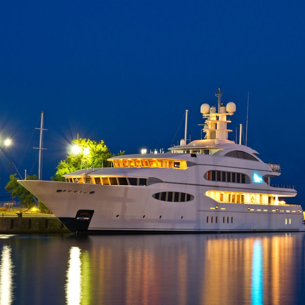 Luxury yacht docked at night with illuminated features, reflecting in the water, symbolizing marine security and maintenance importance for yacht alarm systems.
