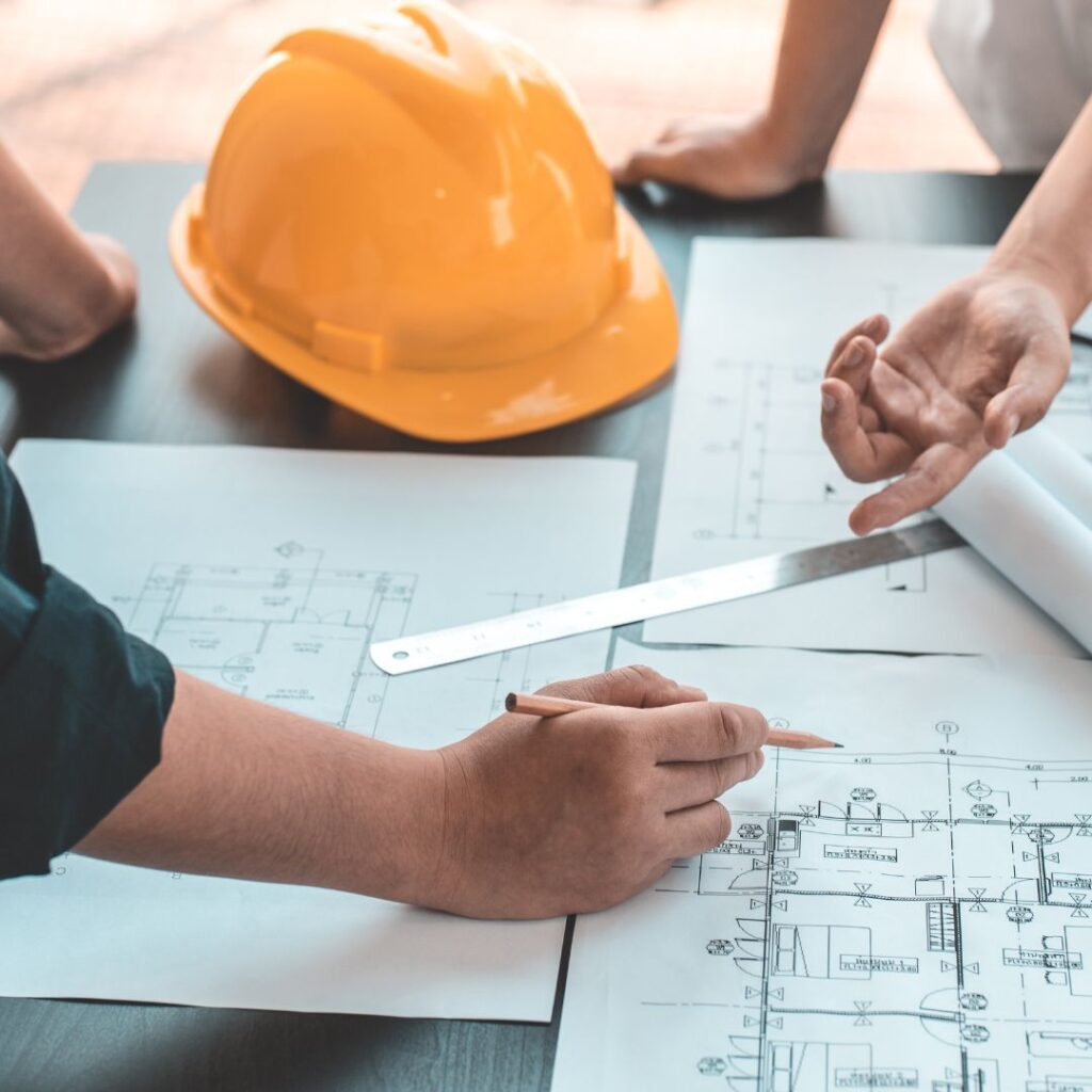 Hands reviewing marine engineering plans with a yellow hard hat and measuring tools on a table, emphasizing TESS LLC's commitment to quality marine repair services.