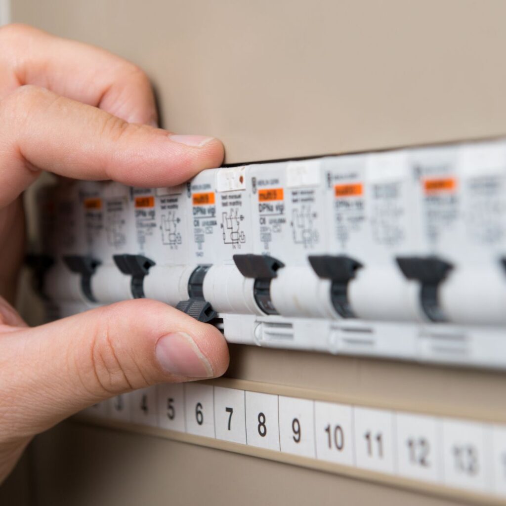 Hand adjusting electrical circuit breakers in a marine panel, showcasing expertise in yacht electrical systems and maintenance.