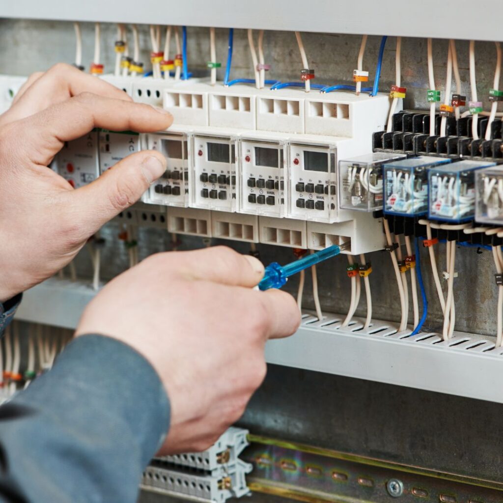 Hands using a screwdriver to inspect and maintain electrical components in a yacht's control panel, emphasizing marine electrical services and efficiency.