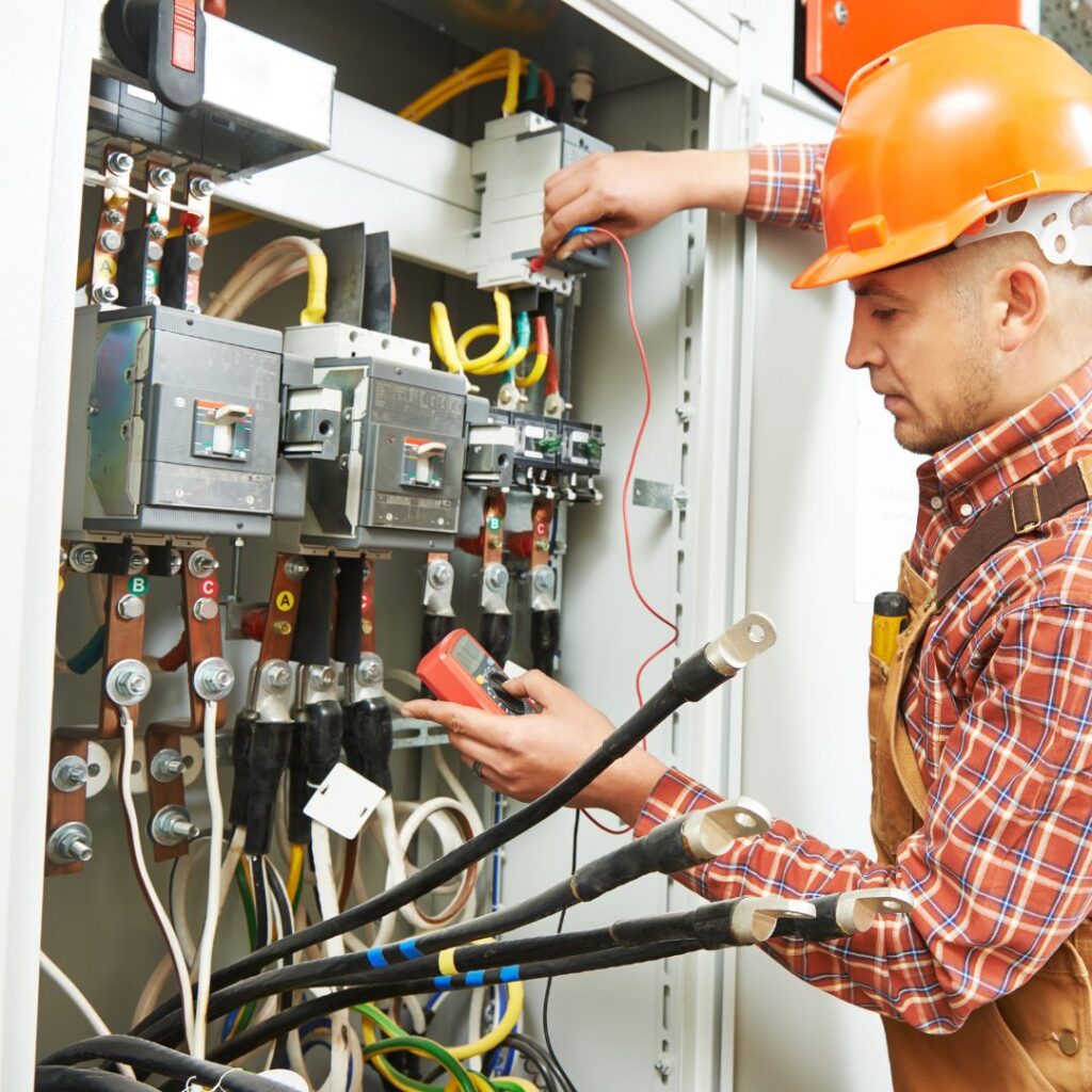 Electrician in hard hat working on marine electrical system panel, testing connections with multimeter, showcasing expertise in yacht electrical design and maintenance.