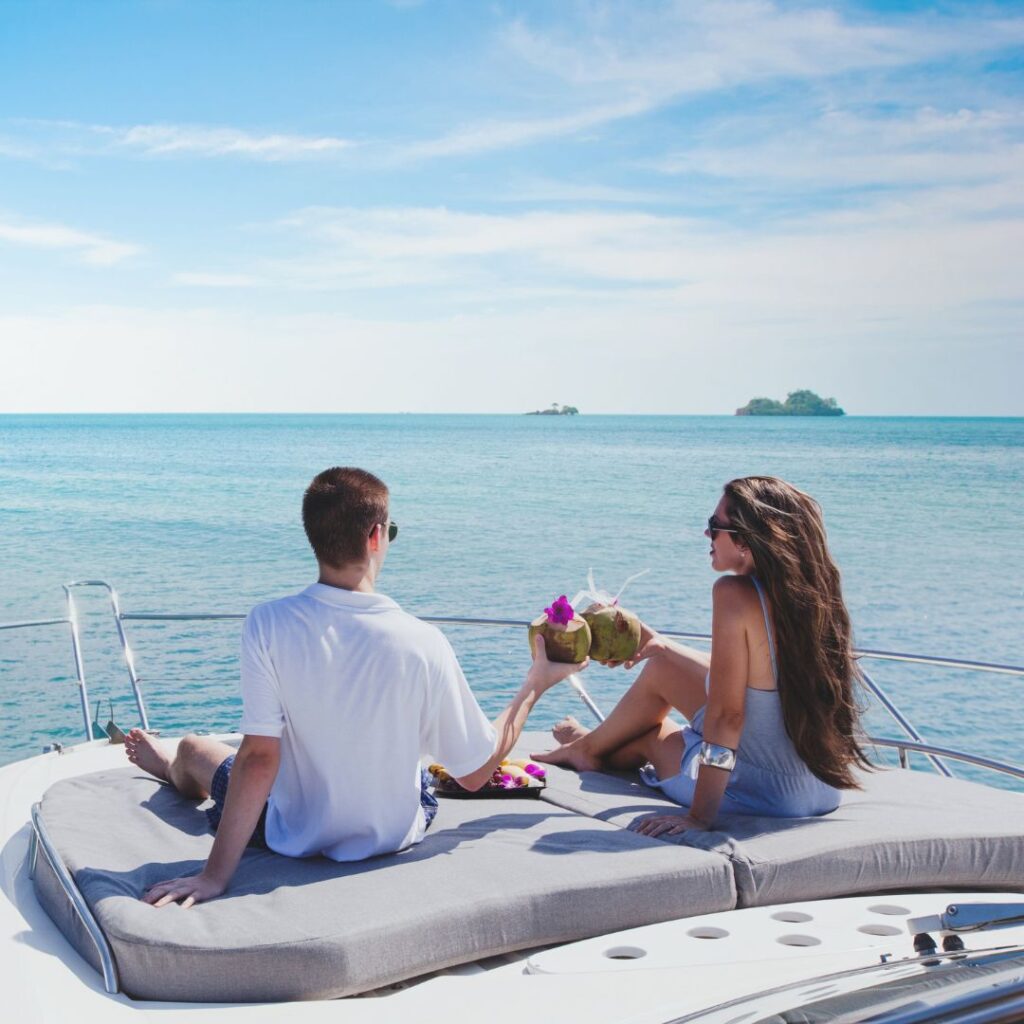 Couple enjoying drinks on a yacht, overlooking calm waters, emphasizing relaxation and luxury in a marine setting.