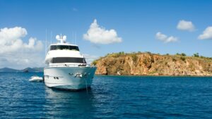 Luxury yacht anchored in clear blue waters near a rocky coastline, highlighting marine elegance and adventure in the context of yacht electrical services.