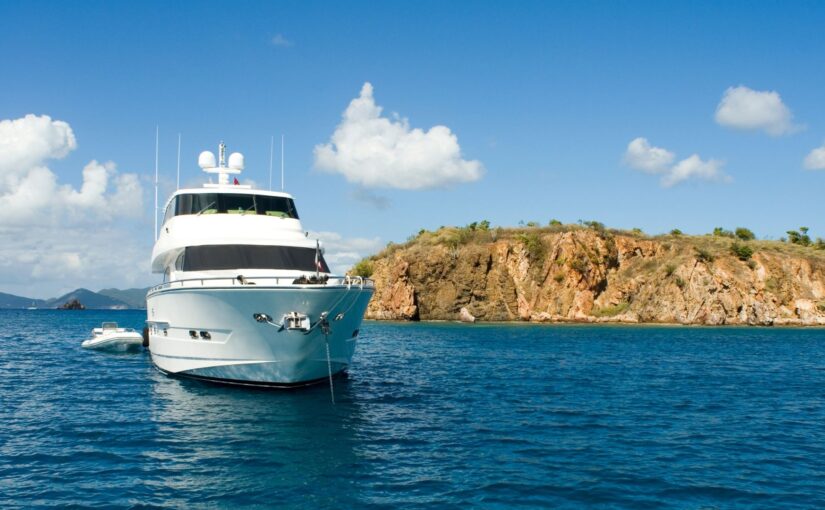 Luxury yacht anchored in clear blue waters near a rocky shoreline, representing common electrical challenges faced by yacht owners.