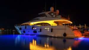 Luxury yacht illuminated at night with vibrant lighting reflecting on water, showcasing advanced marine electrical systems and aesthetic upgrades.