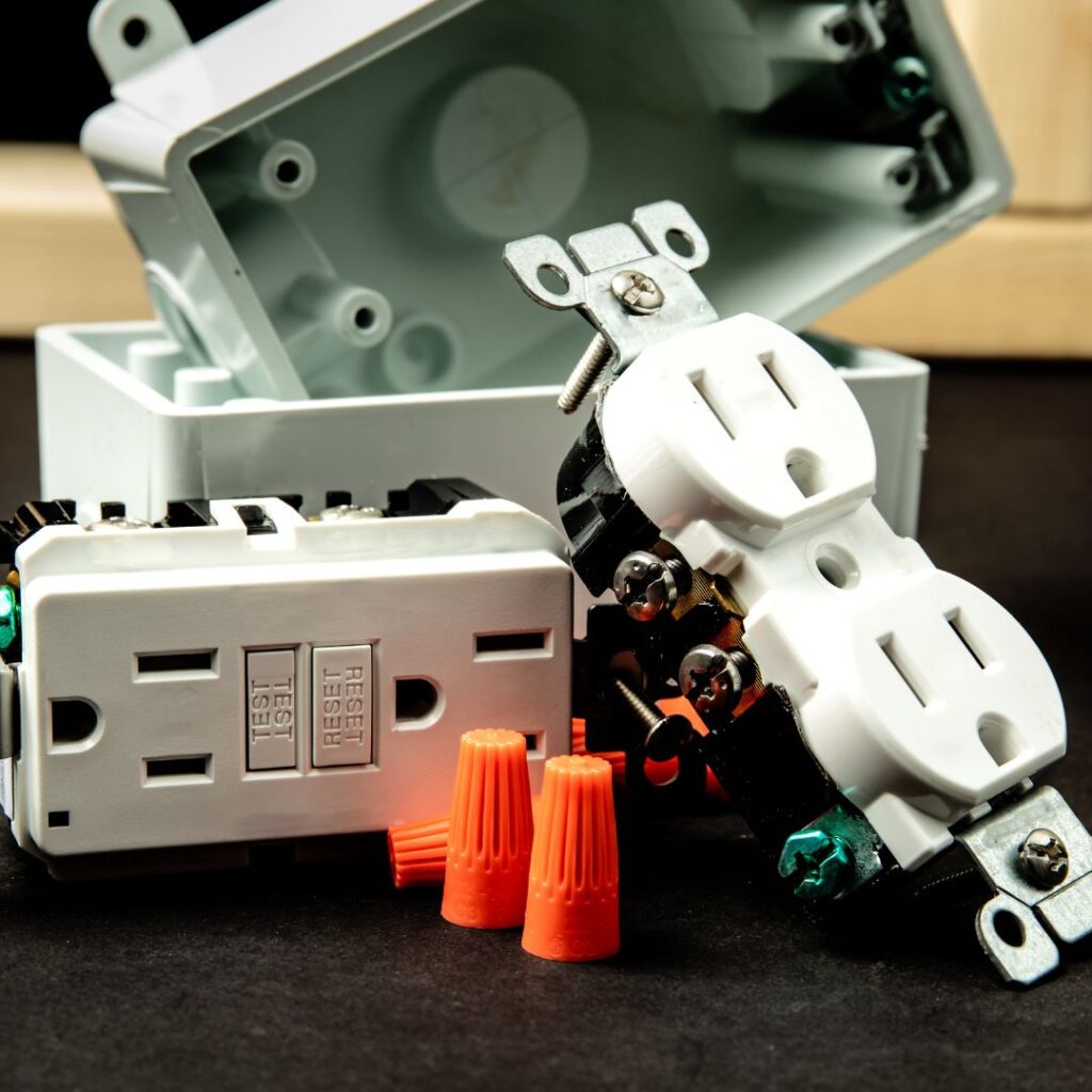 Electrical components including Ground Fault Circuit Interrupter (GFCI) outlet, orange wire connectors, and an open electrical box, emphasizing safety measures for yacht electrical systems.