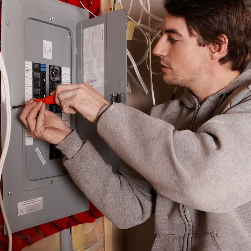 Man working on a yacht electrical panel, using a screwdriver to adjust circuit breakers, emphasizing expertise in marine electrical services.