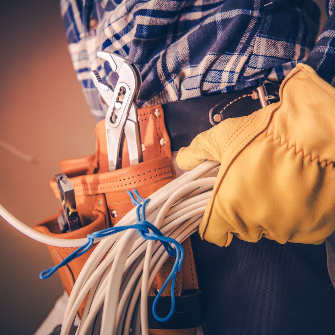 Electrician holding bundled electrical wires and tools in a work belt, emphasizing marine electrical maintenance for yacht safety in Savannah, GA.