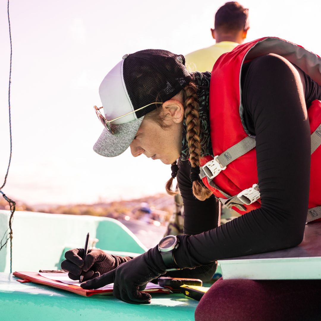 Woman in a life jacket writing notes on a clipboard while onboard a boat, emphasizing safety and precision in yacht electrical upgrades and installations.