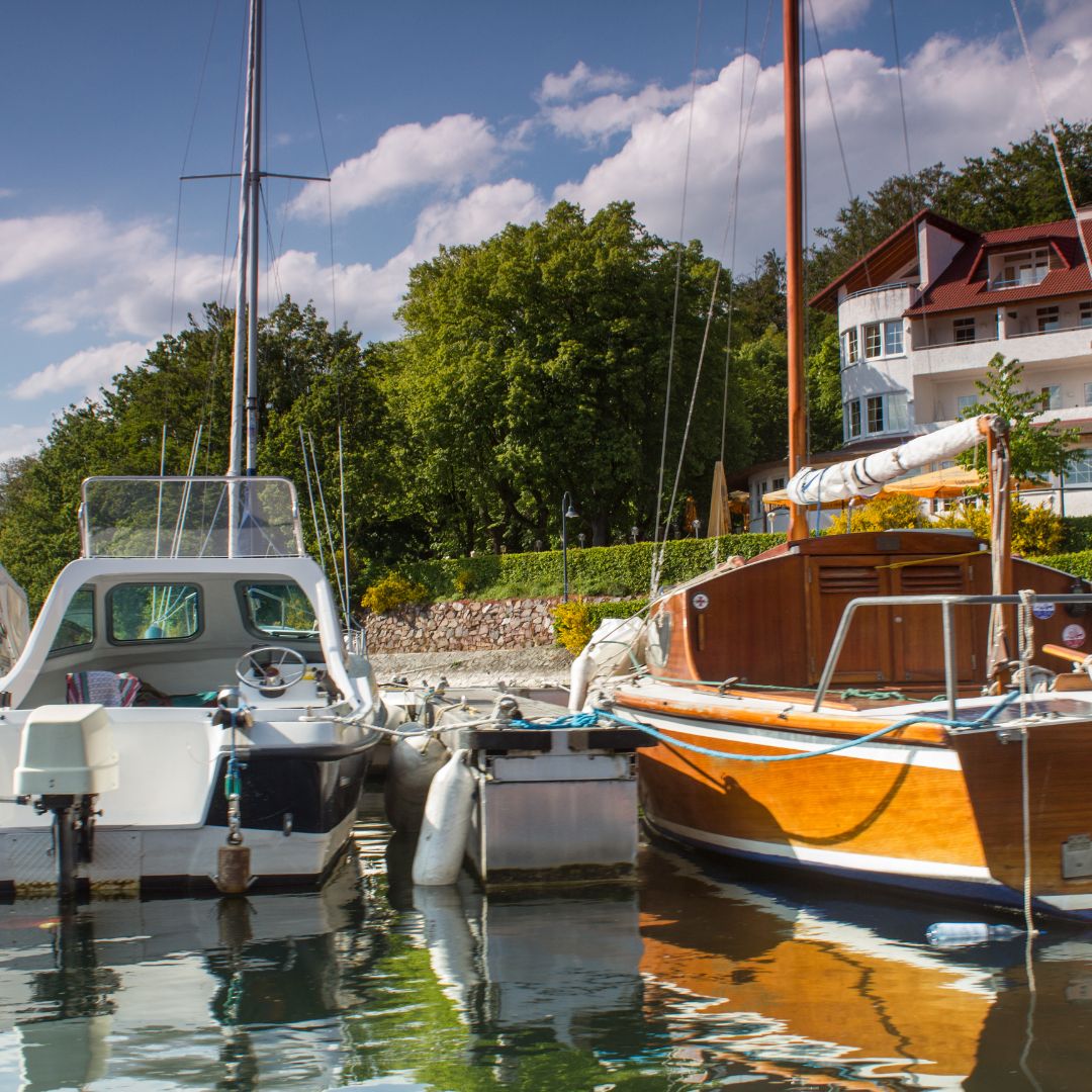 Boats docked in a marina with lush greenery and residential buildings in the background, illustrating the importance of maintaining yacht electrical systems for optimal performance.